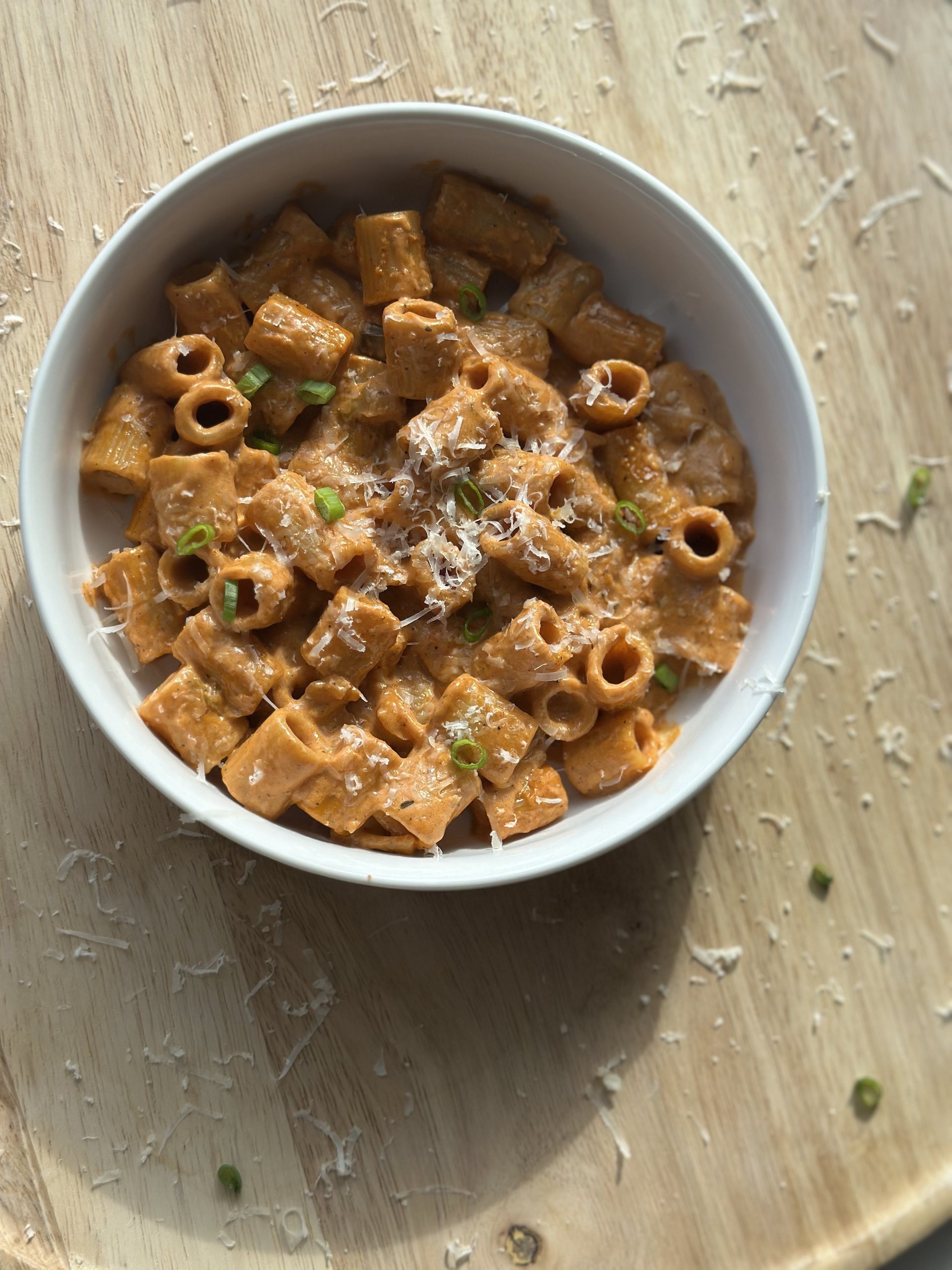 Overhead view of creamy Penne alla Rum with rigatoni pasta, Parmesan, and scallions in a white bowl