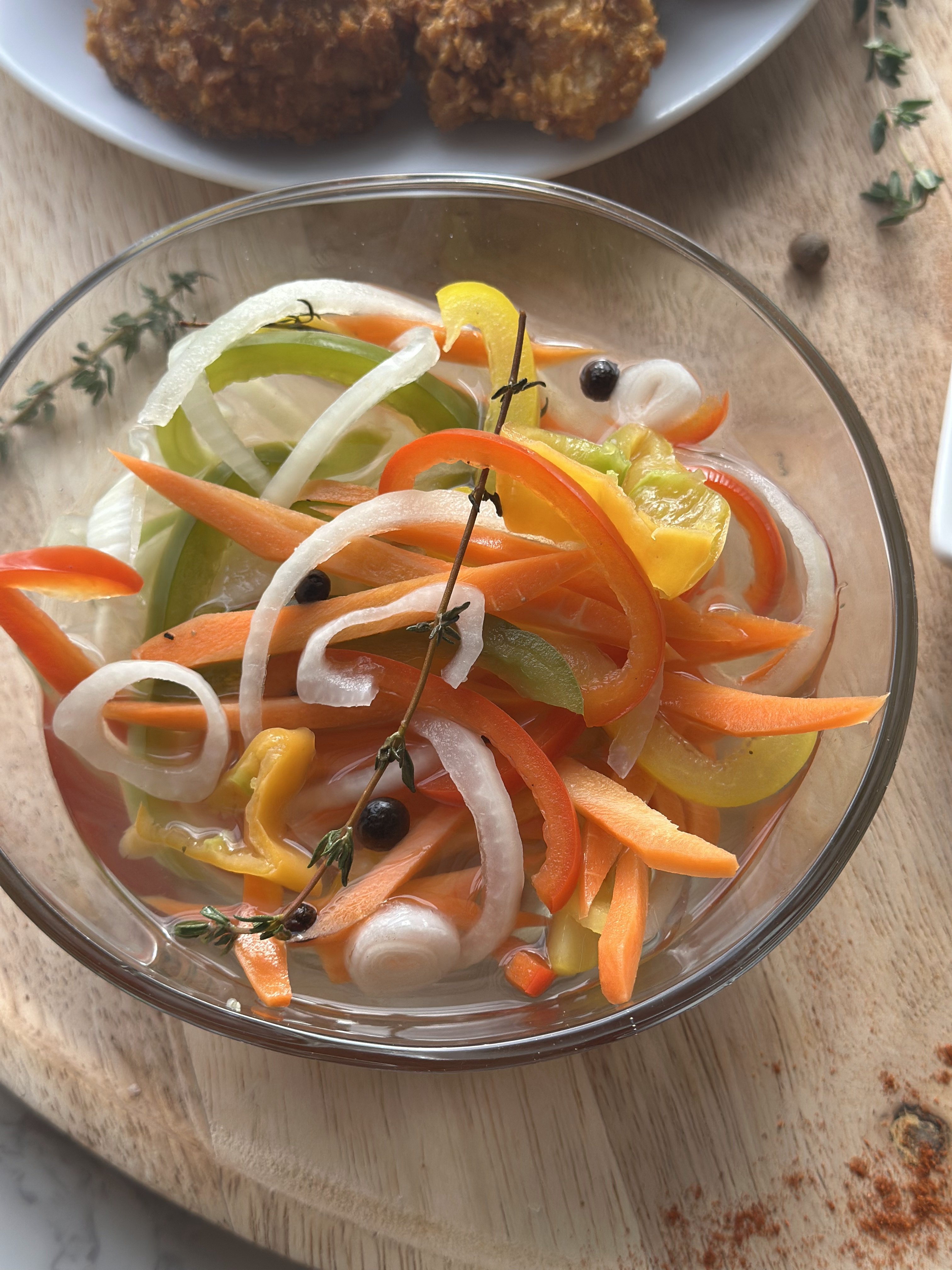 Jamaican escovitch pickle sauce in a glass bowl with julienned carrot, white onion, sweet peppers and thyme, served beside crispy fried fish